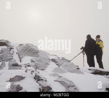 Gli escursionisti e appassionati di fotografia soggiorno sul picco innevato al treppiede. Gli uomini sulla scogliera di parlare e pensare. Inverno da sogno paesaggio con misty sunrise Foto Stock
