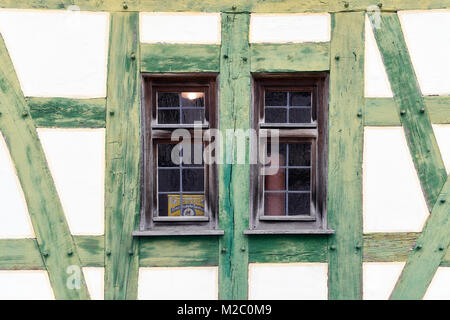 Un primo piano di due piccole finestre in una casa con travi di legno verdi. Il legno vecchio e il design semplice danno alla casa un aspetto rustico e rurale. Foto Stock