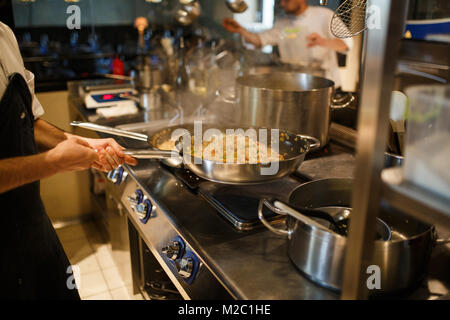 L'uomo cuoco prepara il riso, il risotto in una grande padella nella cucina del ristorante Foto Stock