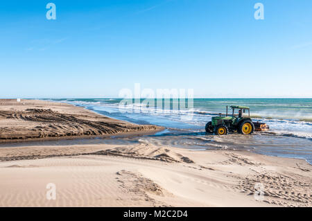 Il trattore trainato beach cleaner rastrellando sabbia di mare, lavorando sulla spiaggia, il delta del fiume Ebro, Catalogna, Spagna Foto Stock