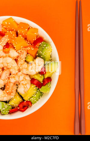 Hawaiian gamberetti o gamberi Poke ciotola con patate dolci di Avocado e cetriolo contro uno sfondo arancione Foto Stock