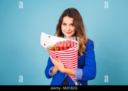 Bouquet di fragole nelle mani di una ragazza su sfondo blu Foto Stock