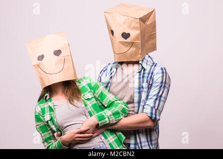 Amore giovane che coprono i loro volti con sacchetto di carta su sfondo bianco Foto Stock