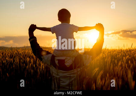 Padre figlio che porta sulle spalle nel campo di grano al tramonto Foto Stock