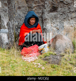Chimborazo, Ecuador, Dicembre 20, 2017: tradizionalmente vestiti donna ecuadoriana sbucciare l'aglio sul lato di una strada Foto Stock