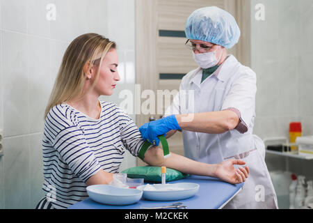 Preparazione per il test del sangue con la giovane e bella donna bionda dal medico donna in camice bianco uniforme medica sul tavolo in bianco e luminosa sala. L'infermiera sfregamento di una sterile a mano del tessuto del paziente. Foto Stock