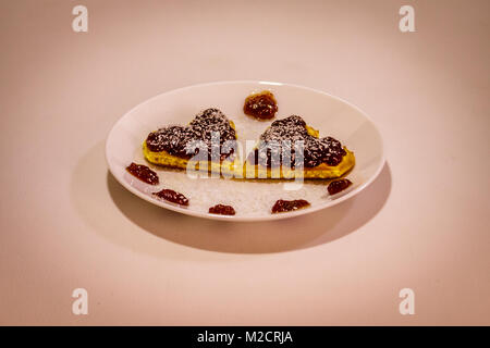 Due a forma di cuore fumetto waffels confettura di fragole e farina di cocco su di loro su sfondo bianco Foto Stock