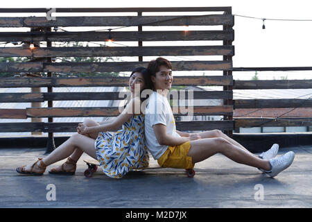 Coppie giovani sedersi su uno skateboard Foto Stock