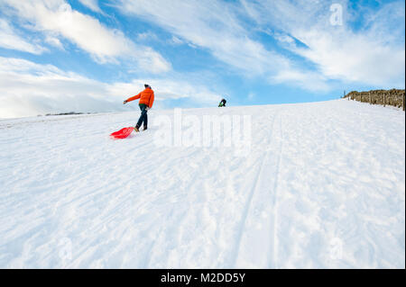 Ragazzo tirando una slitta nella neve fino hill Foto Stock