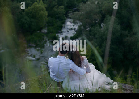 Caucasian sposa e lo sposo seduto su di una collina ad ammirare il fiume Foto Stock