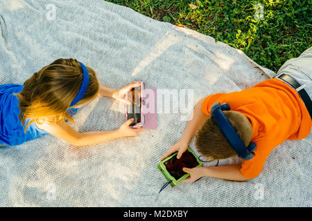 Caucasian fratello e sorella di posa sulla coperta utilizzando la tecnologia Foto Stock