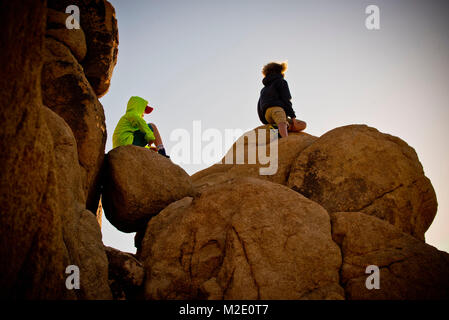 Ragazzi seduti sulle rocce sotto il cielo blu Foto Stock