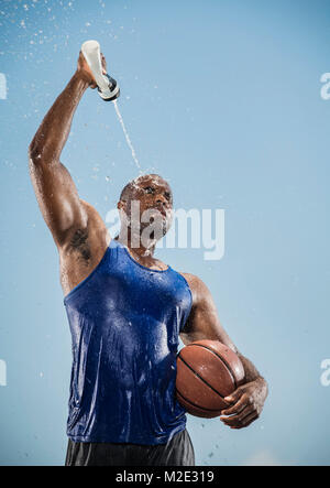 Uomo nero tenendo la pallacanestro il raffreddamento con acqua in bottiglia Foto Stock