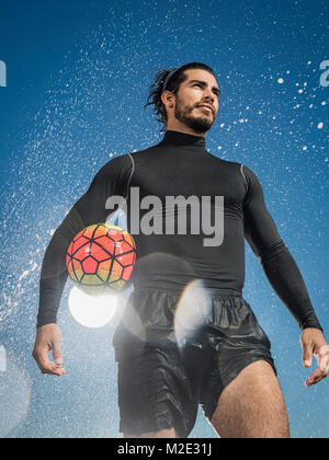 Spruzzi d'acqua su uomo ispanico tenendo palla calcio Foto Stock