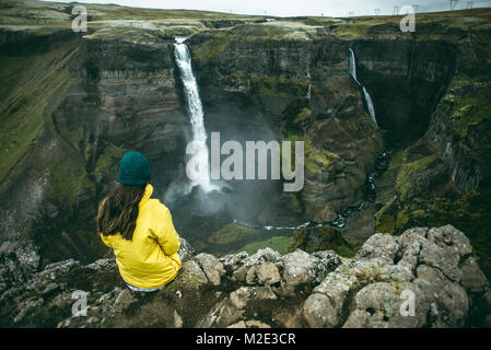 Caucasian donna seduta sulla scogliera ammirando le cascate Foto Stock