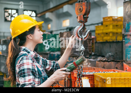 Giovane e bella macchina fresatrice factory lavoratore di sesso femminile che la regolazione della catena di lavorazione gru la preparazione di Tornio per la spedizione di prodotti finiti. Foto Stock