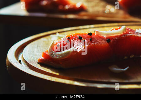 Condite il salmone con cipolla, pepe nero, cipolla sul tagliere Foto Stock