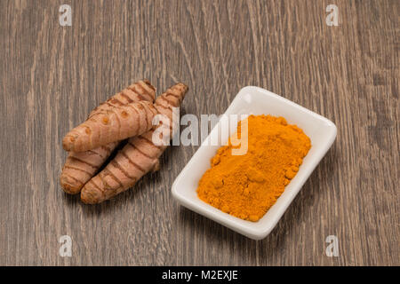 La curcuma in polvere con la curcuma root su uno sfondo di legno Foto Stock