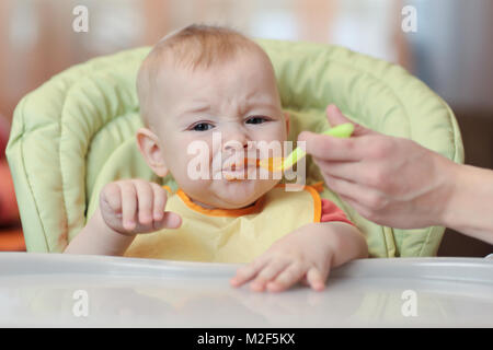 Carino Il bambino rifiuta di mangiare cibo dal cucchiaio con la faccia sporca di purea di verdure. Foto Stock