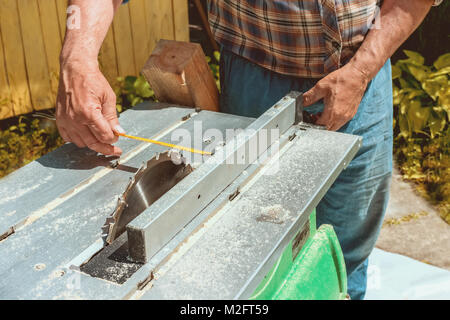 Maschio lato rende la misurazione con un metro a nastro e sega circolare taglia un pezzo di cartone in una giornata di sole. Un telaio orizzontale. Foto Stock