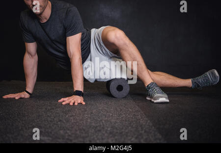 Athletic uomo usando un rullo in gomma spugna per alleviare muscoli doloranti dopo un allenamento. Foto Stock
