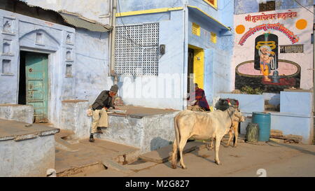 CHITTORGARH, Rajasthan, India - 14 dicembre 2017: scene di strada con una vacca e due uomini godendo il sole in fronte di colorate case tradizionali Foto Stock