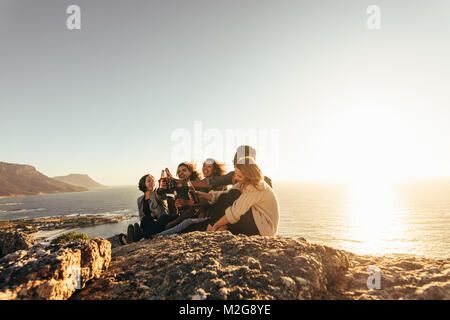 Amici seduti sulla montagna e birre di tostatura durante il tramonto. Un gruppo di uomini e donne festa all'aperto durante il tramonto. Foto Stock