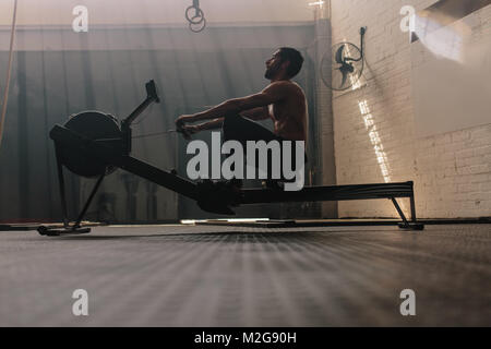 Maschio muscolare utilizzando vogatore in palestra. Montare l'uomo facendo allenamento nel centro fitness. Foto Stock