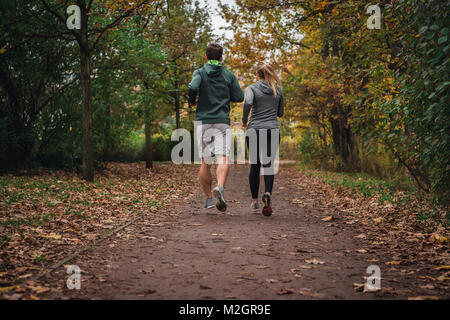 Uomo caucasico e la donna che corre attraverso il parco in autunno caduta stagione in discesa su un sentiero di vuoto. Foto Stock