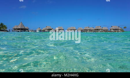 Resort tropicale con bungalow con tetto in paglia in laguna visto dalla superficie del mare, Tikehau Atoll, Tuamotus, Polinesia francese, oceano pacifico, Oceania Foto Stock