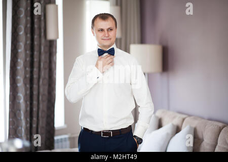 L uomo lo sposo in camicia bianca mettendo sul tirante butterfly Foto Stock