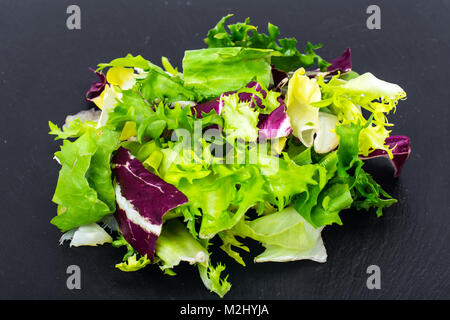 Concetto di pasto sano. Le foglie fresche di diverse insalate su nero Foto Stock