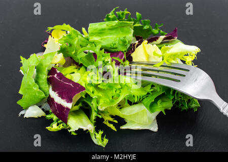 Concetto di pasto sano. Le foglie fresche di diverse insalate su nero Foto Stock