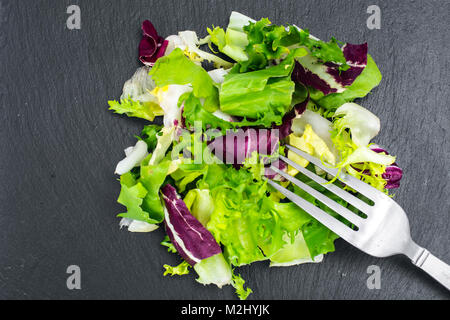 Concetto di pasto sano. Le foglie fresche di diverse insalate su nero Foto Stock