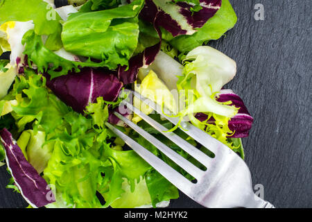 Concetto di pasto sano. Le foglie fresche di diverse insalate su nero Foto Stock