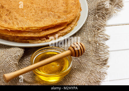 Frittelle su una piastra bianca. Miele di fresco in un barattolo. Cucchiaio di legno per il miele. Il dessert. Una sana prima colazione. Il tavolo era ricoperto di tela. Foto Stock