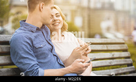 Maschio e femmina seduta sul banco da lavoro con telefoni cellulari, sorridente e divertirsi, stock video Foto Stock