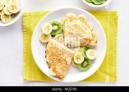 Crepes con banana e kiwi fette sulla piastra. Vista superiore, laici piatta Foto Stock