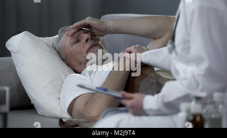 Ritirato uomo disteso nel letto e lamentando il medico per il mal di testa ad alta temperatura, stock footage Foto Stock