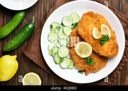 Cotoletta con insalata di cetrioli su piastra su un tavolo di legno. Vista superiore, laici piatta Foto Stock