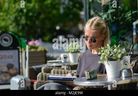 Una bionda studente la lettura di un libro mentre avente un caffè al mattino. Oslo, Norvegia Foto Stock