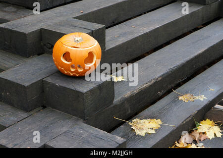 La zucca scolpita con gli occhi e la bocca su di un nero scala in legno. La mattina dopo la festa di Halloween Foto Stock