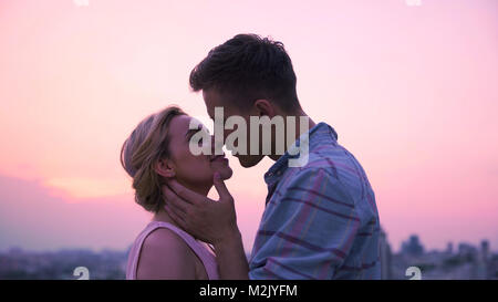 Amare giovane appassionatamente kissing, meeting Alba sul tetto di un edificio alto Foto Stock