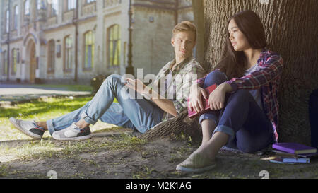 Guy sotto agli alberi guardando alla ragazza seduta accanto a lui, amore a prima vista i sentimenti Foto Stock