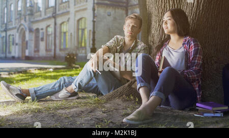 Multirazziale studenti maschi e femmine seduto sotto agli alberi, guardando al futuro, il futuro Foto Stock