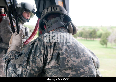 Un membro della 45th della brigata di fanteria combattere Team guarda oltre il bordo di un UH-60 Black Hawk elicottero durante air assault formazione ospitato da Oklahoma Guardia Nazionale a Camp Gruber, Okla. I soldati e gli avieri dell'Air Assault Course sono attesi a rappel da circa 100 al di sopra del suolo per completare con successo il corso di formazione. Air Assault Rappel giorno 07 da Oklahoma Guardia Nazionale Foto Stock