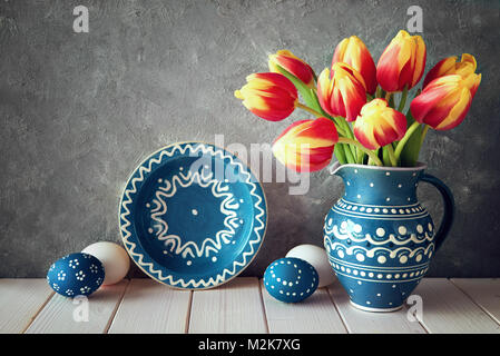 Rosso-tulipani gialli in ceramica blu brocca con uova di Pasqua e di una lavagna nera su sfondo grigio Foto Stock