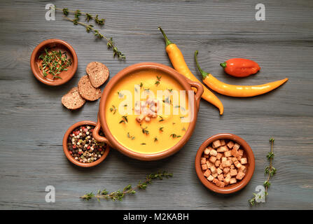 Zuppa di zucca in vaso in ceramica su grigio legno rustico servita con timo e crostini. Accanto ad essa sono il peperoncino, foglie di timo e crostini. Piatto, laici vi Foto Stock