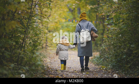 Gioiosa bambina con la sua mamma e Teddy Bear passeggiate nel parco di autunno, vista posteriore Foto Stock