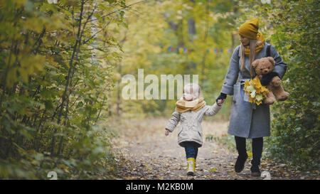 Gioiosa bambina con la sua mamma e Teddy Bear passeggiate nel parco di autunno Foto Stock